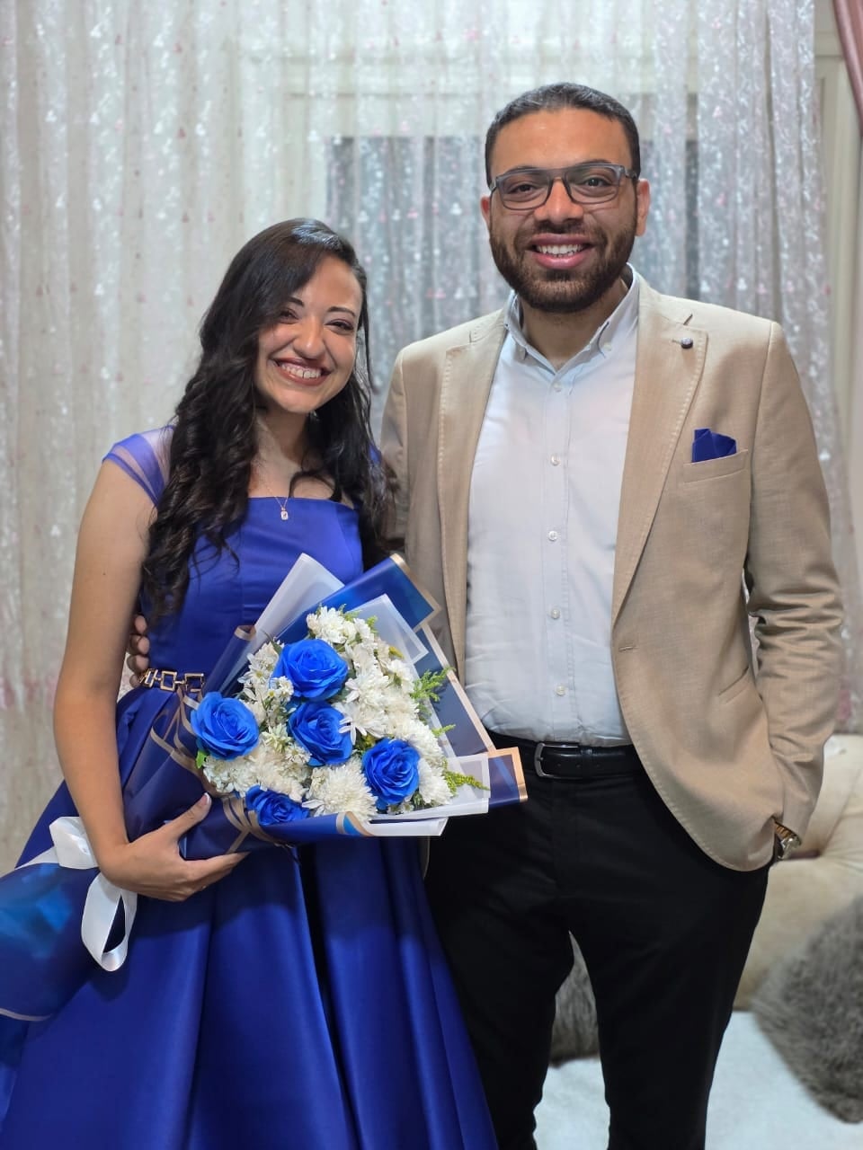 Nada in a royal-blue dress holding blue roses beside John on their engagement day